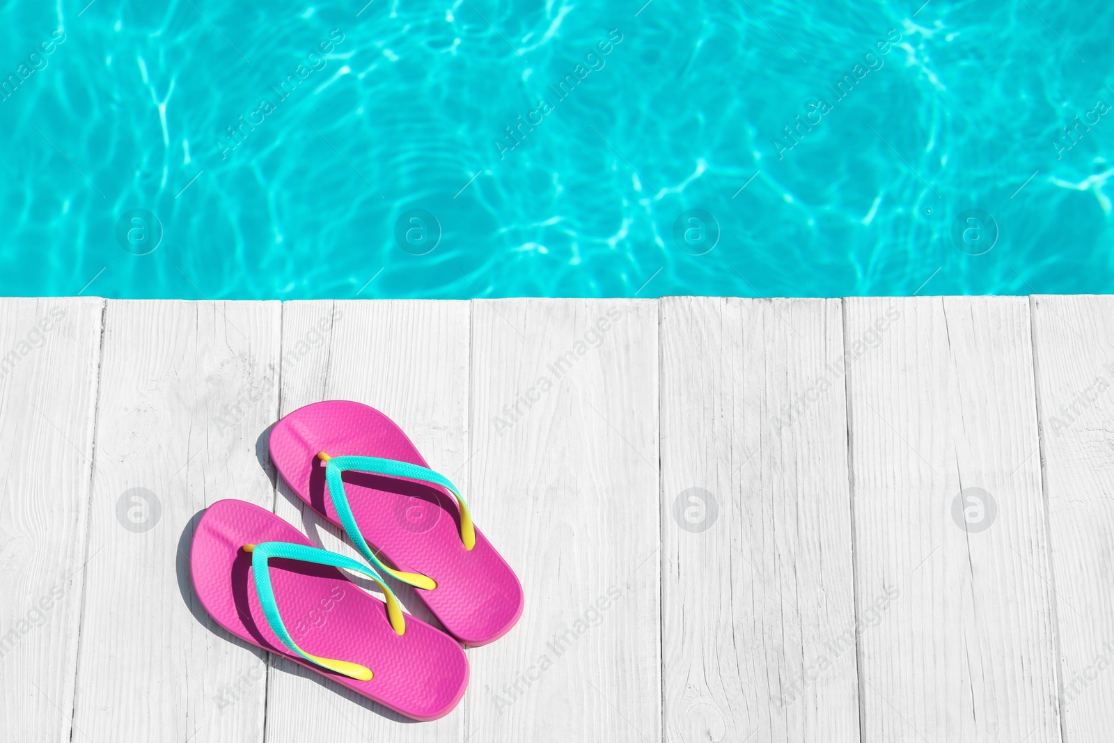 Photo of Slippers on wooden deck near swimming pool, top view with space for text. Beach accessory