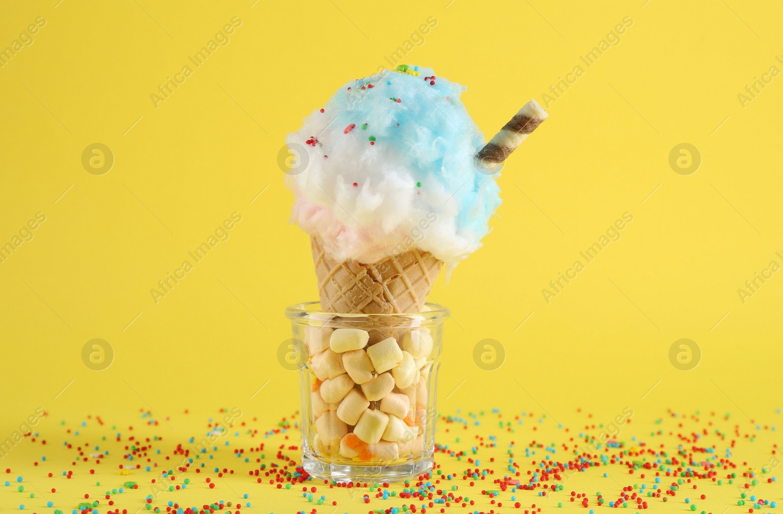 Photo of Sweet cotton candy in waffle cone on yellow background, closeup