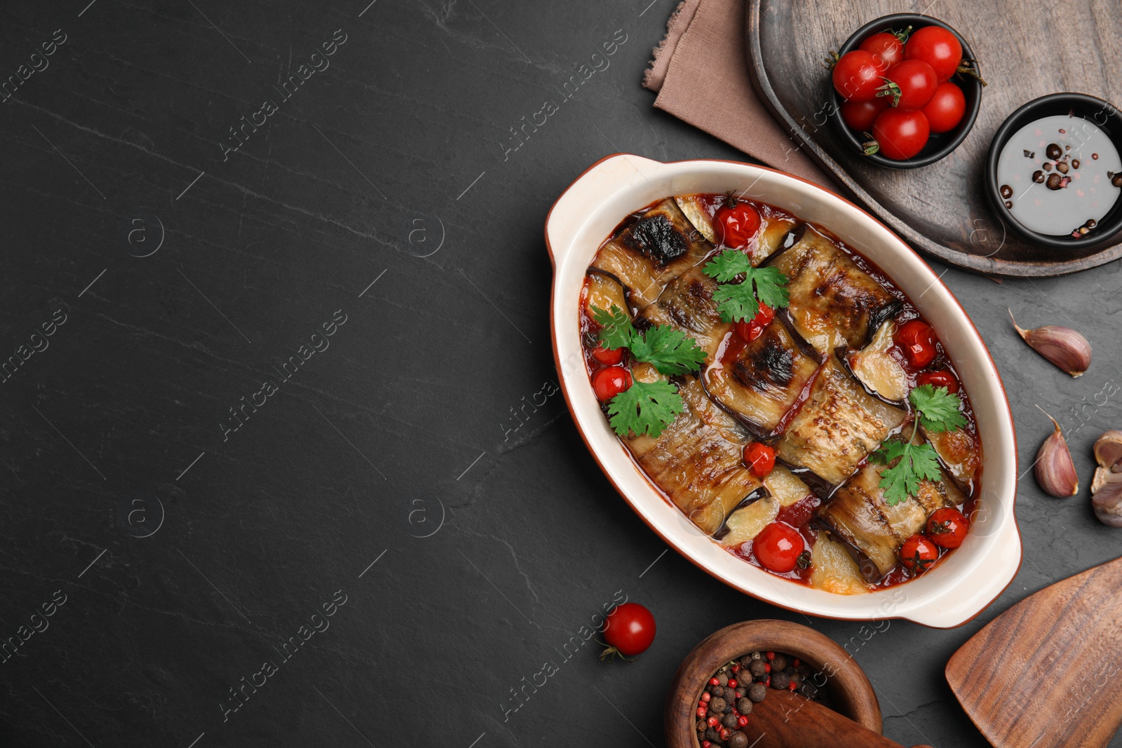 Photo of Tasty eggplant rolls with tomatoes, cheese and parsley in baking dish on black table, flat lay. Space for text