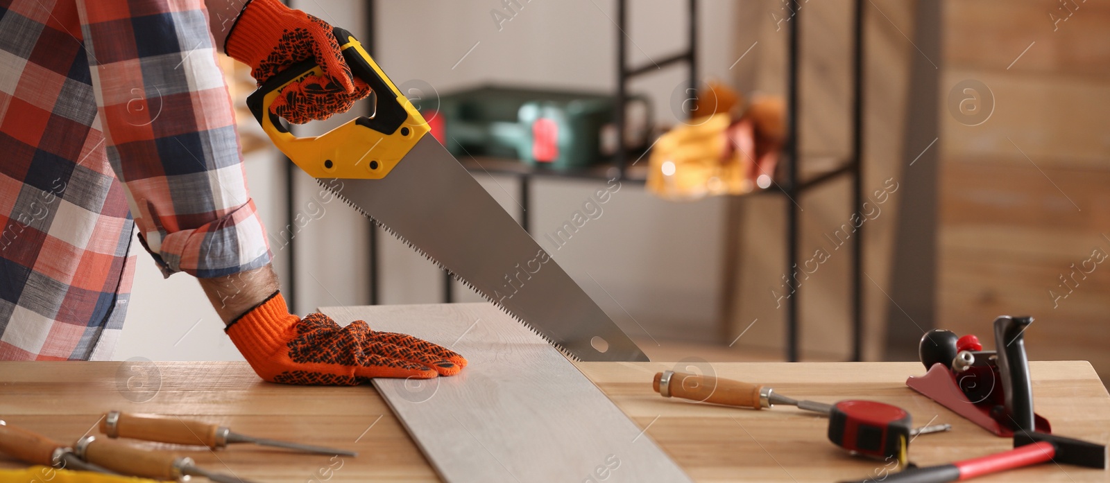 Image of Carpenter sawing wooden plank at table in workshop, closeup. Banner design