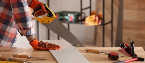 Image of Carpenter sawing wooden plank at table in workshop, closeup. Banner design