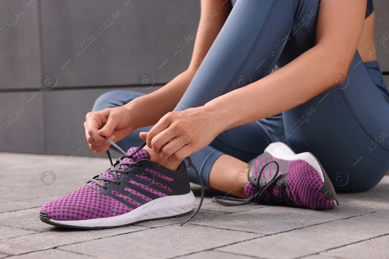 Photo of Woman tying shoelace of sneakers on street, closeup