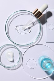 Petri dishes with samples of cosmetic serums, bottle and pipette on white background, flat lay