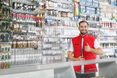 Photo of Salesman standing near showcase with fishing equipment in sports shop. Space for text