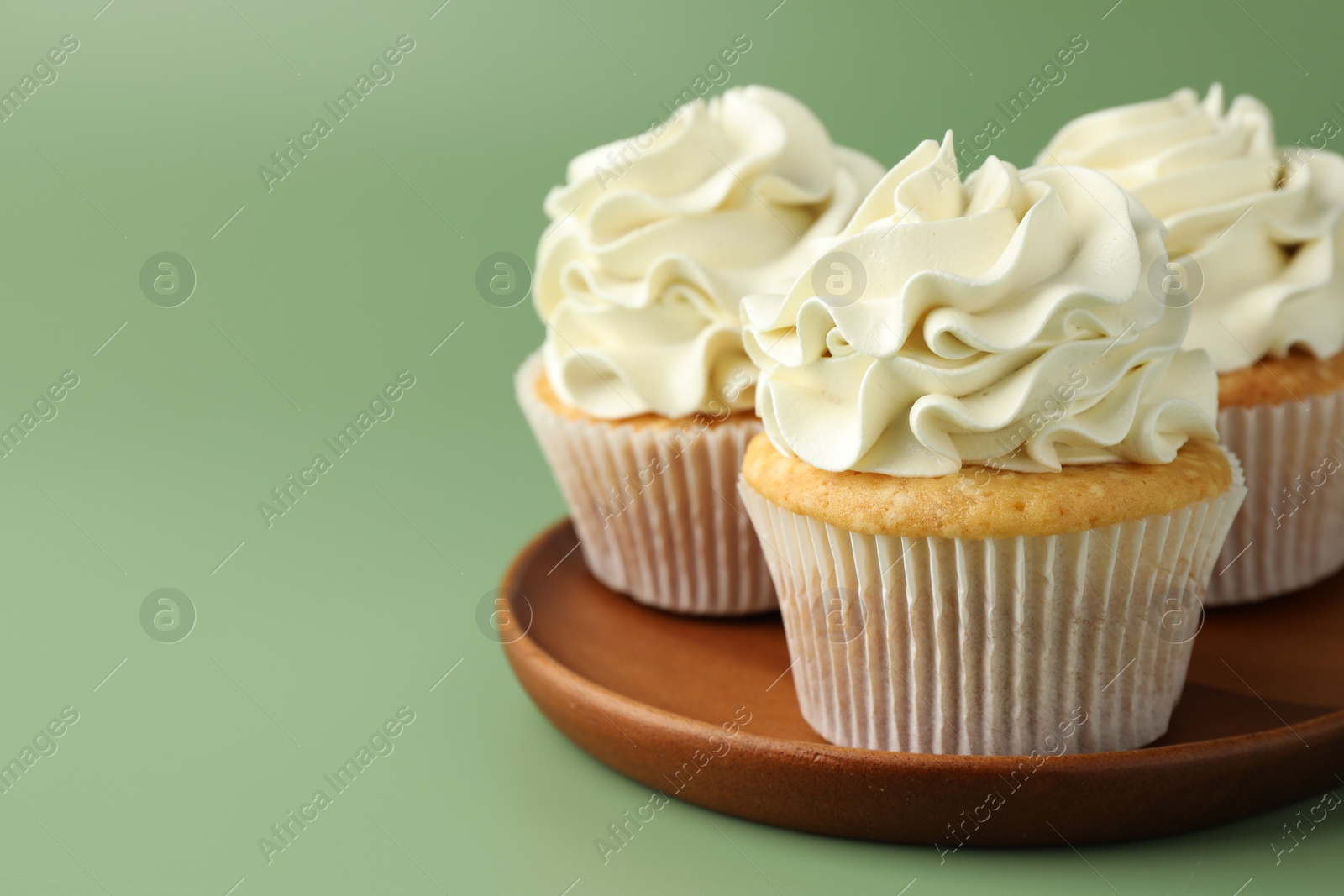 Photo of Tasty vanilla cupcakes with cream on green background, closeup. Space for text