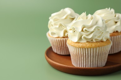 Tasty vanilla cupcakes with cream on green background, closeup. Space for text