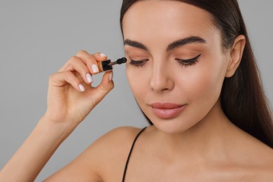 Photo of Beautiful young woman applying mascara on grey background, closeup