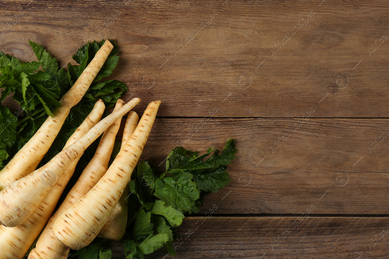 Photo of Fresh ripe parsnips with leaves on wooden table, flat lay. Space for text