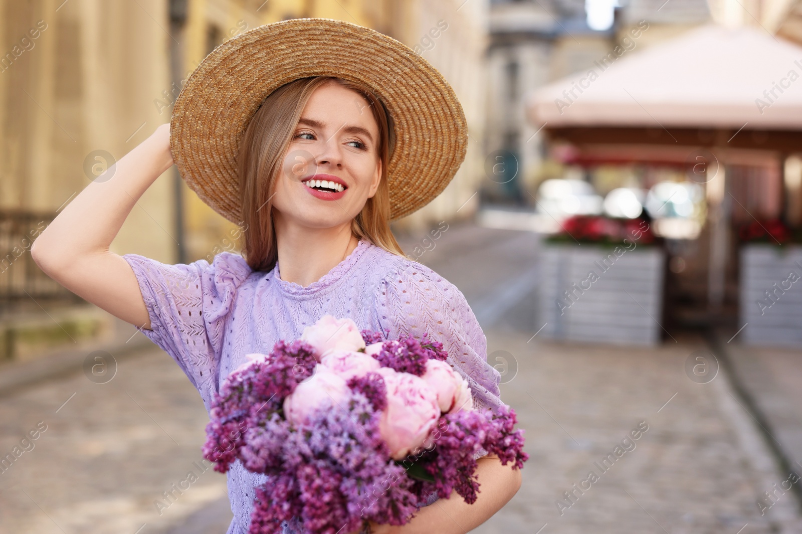 Photo of Beautiful woman with bouquet of spring flowers on city street, space for text