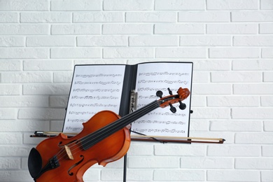 Violin and note stand with music sheets on brick wall background