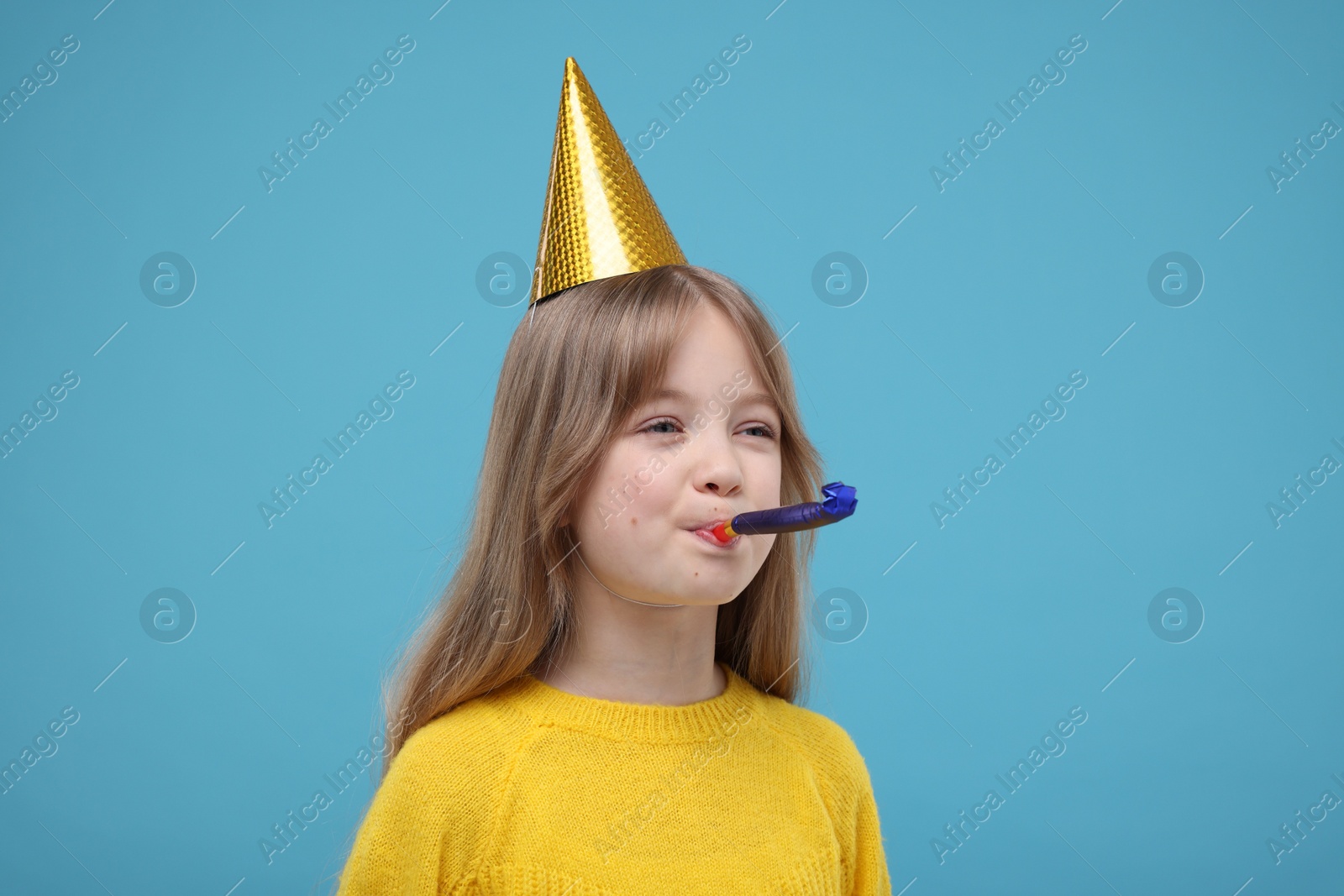 Photo of Cute little girl in party hat with blower on light blue background