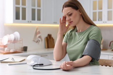 Photo of Woman suffering from headache and measuring blood pressure in kitchen, space for text