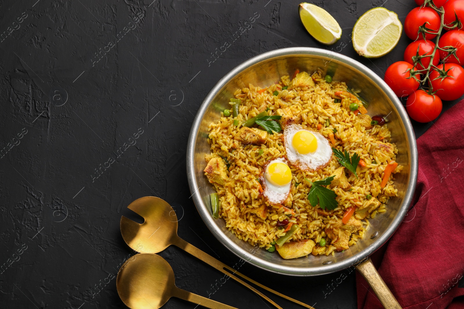 Photo of Tasty rice with meat, eggs and vegetables in frying pan near products on black textured table, flat lay. Space for text