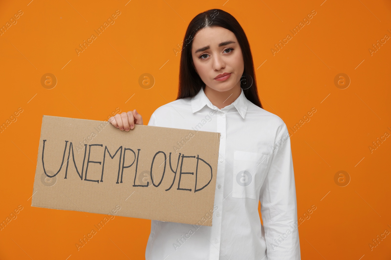 Photo of Young woman holding sign with word Unemployed on orange background