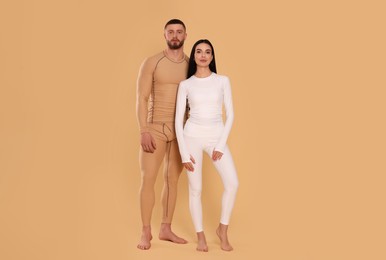 Photo of Man and woman in warm thermal underwear on beige background. Space for text