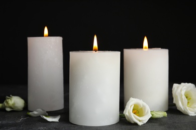 Burning candles and flowers on grey table against black background