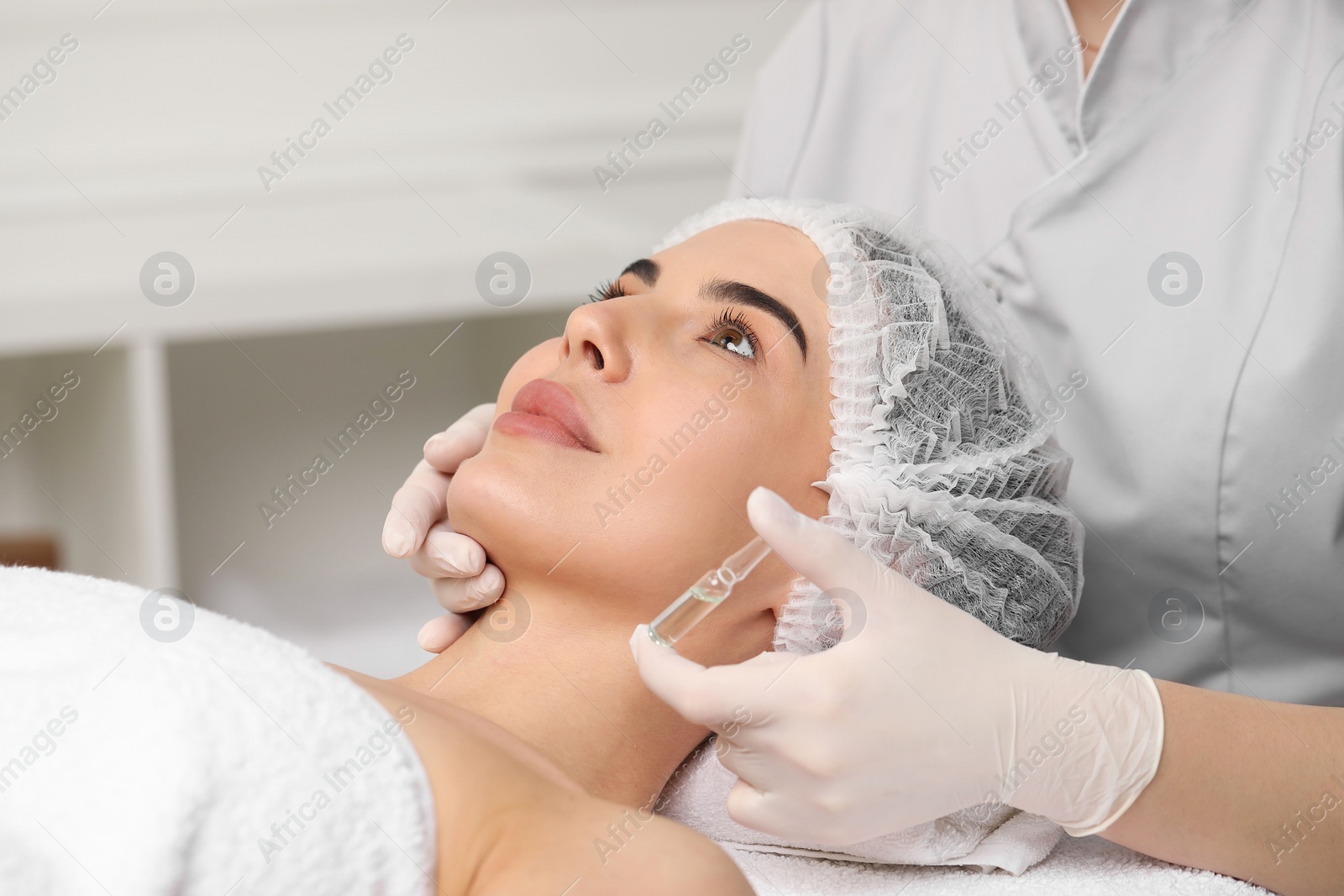 Photo of Professional cosmetologist holding skincare ampoule while working with client in clinic, closeup