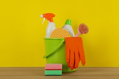 Photo of Bucket with different cleaning supplies on wooden floor near yellow wall