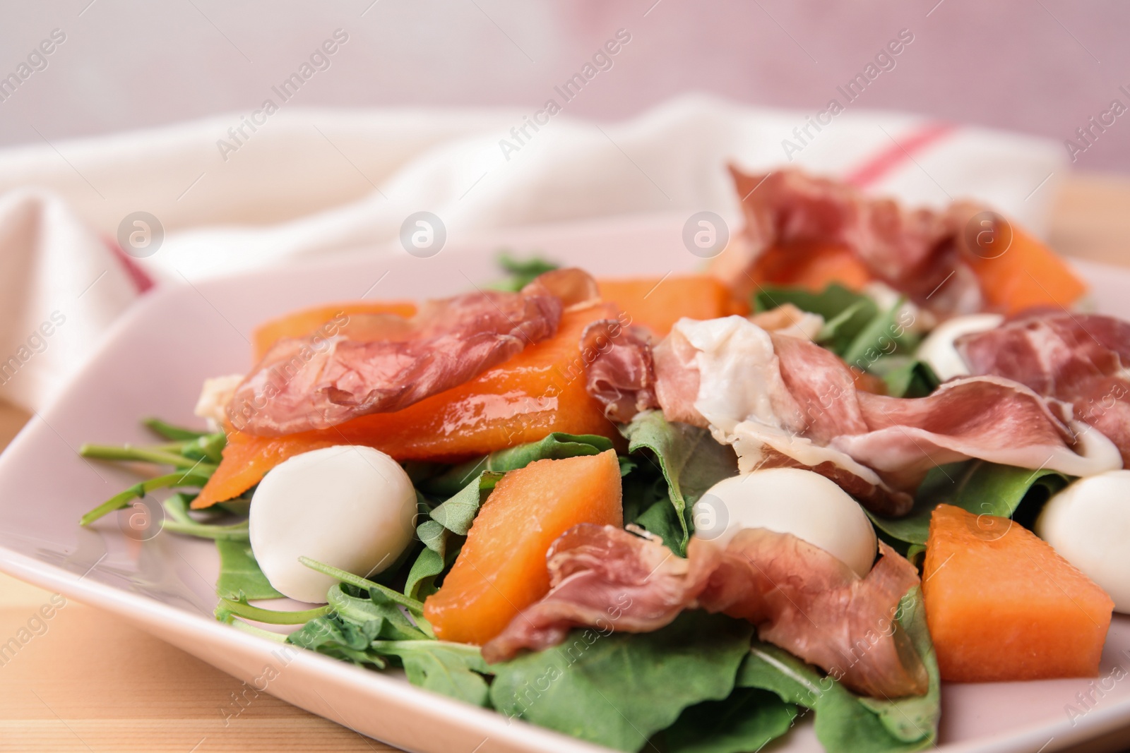 Photo of Fresh melon with prosciutto, mozzarella and arugula on plate, closeup