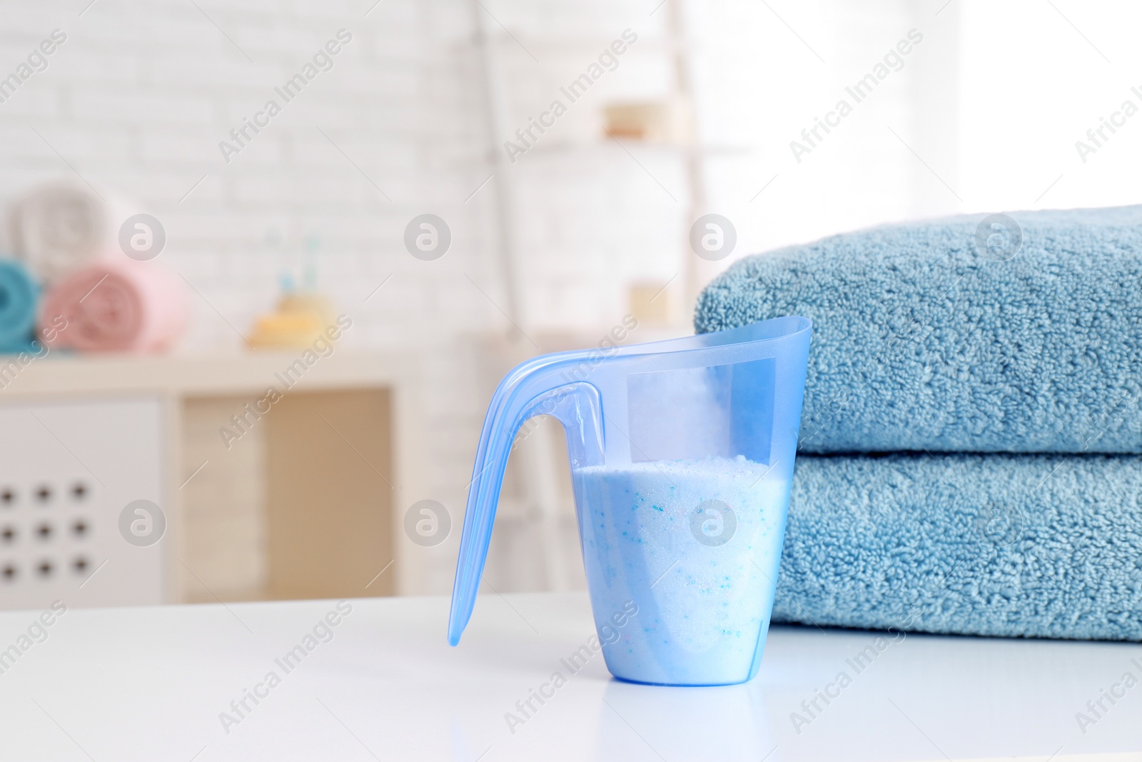 Photo of Measuring cup with washing powder and clean towels on table indoors, space for text. Laundry day