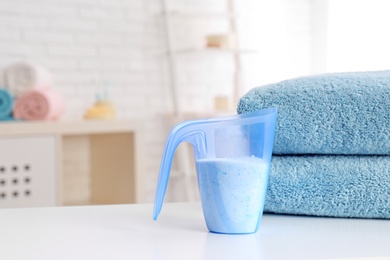 Photo of Measuring cup with washing powder and clean towels on table indoors, space for text. Laundry day