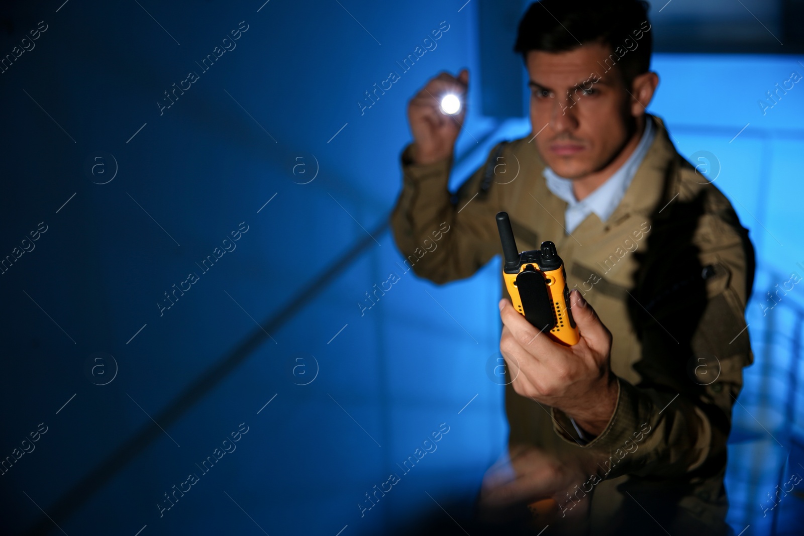 Photo of Professional security guard with portable radio set in dark room, focus on hand