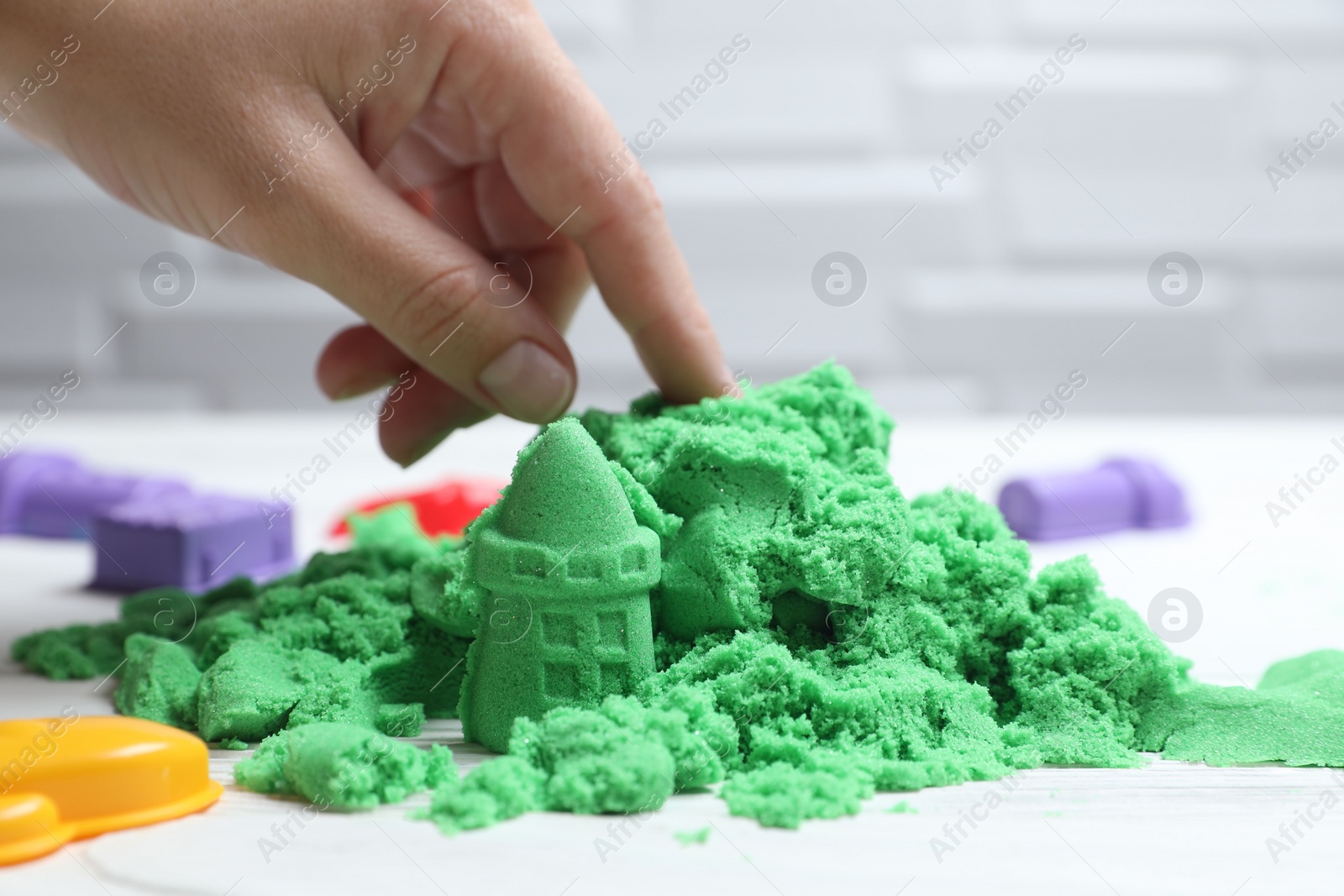 Photo of Woman playing with green kinetic sand at white table, closeup