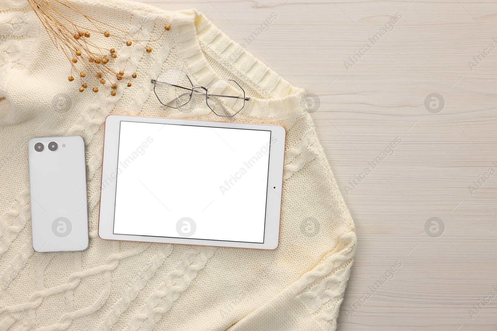 Photo of Modern tablet, glasses, smartphone and sweater on white wooden table, flat lay. Space for text