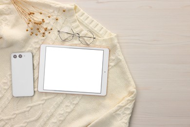 Modern tablet, glasses, smartphone and sweater on white wooden table, flat lay. Space for text