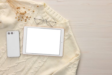 Photo of Modern tablet, glasses, smartphone and sweater on white wooden table, flat lay. Space for text