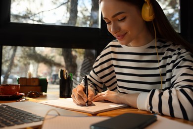 Photo of Young female student with laptop and headphones studying at table in cafe