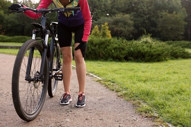 Photo of Woman with injured knee and bicycle outdoors, closeup. Space for text