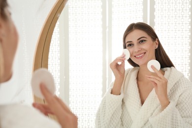 Young woman with cotton pads cleaning her face near mirror in bathroom