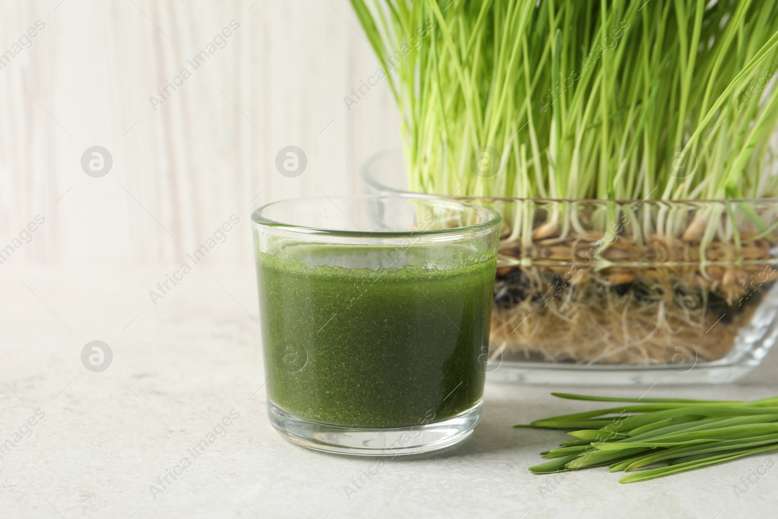 Photo of Wheat grass drink in glass and fresh sprouts on light table