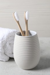 Photo of Bamboo toothbrushes in holder and soft towel on light grey table