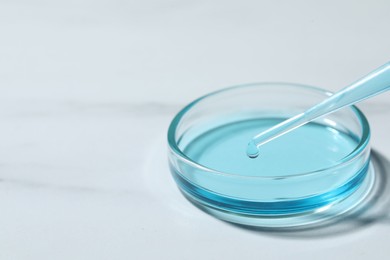 Photo of Dripping liquid from pipette into petri dish at white table, closeup. Space for text