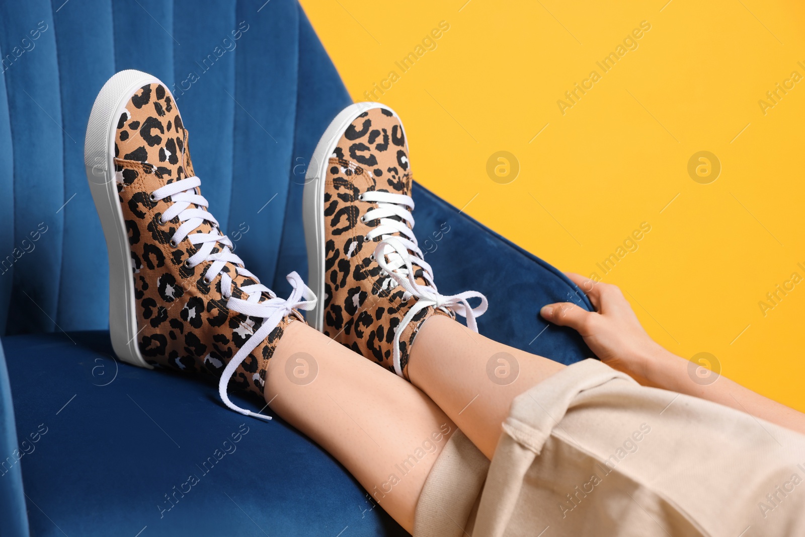 Photo of Woman posing in classic old school sneakers with leopard print and armchair on orange background, closeup