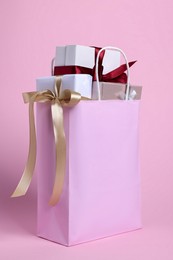 Photo of Color paper shopping bag full of gift boxes on pink background