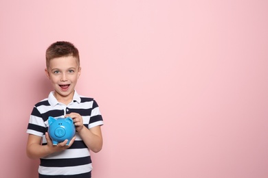Photo of Emotional little boy with piggy bank on color background. Space for text