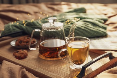 Wooden tray with freshly brewed tea and cookies on bed in room. Cozy home atmosphere