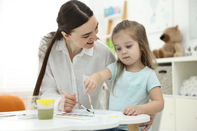 Mother and her little daughter painting with watercolor at home