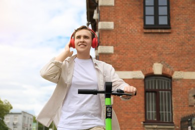 Photo of Handsome young man with headphones riding electric scooter on city street