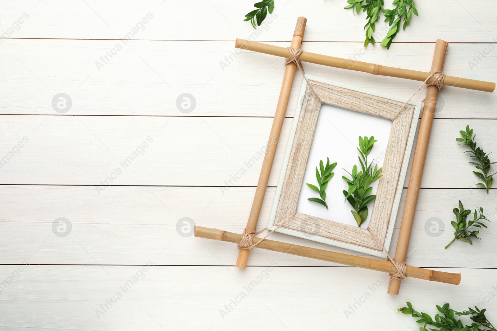 Photo of Flat lay composition with bamboo frame and green leaves on white wooden table. Space for text