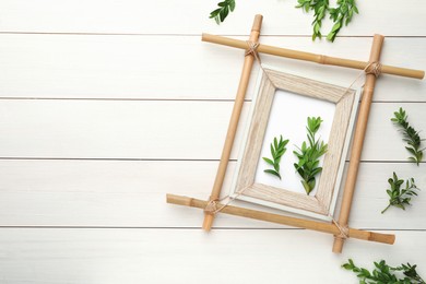 Photo of Flat lay composition with bamboo frame and green leaves on white wooden table. Space for text