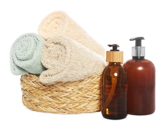 Soft towels in wicker basket and bottles of cosmetic products on white background