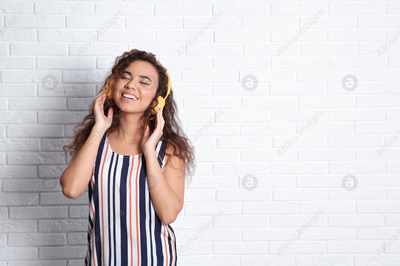 Photo of African-American woman listening to music with headphones near brick wall, space for text