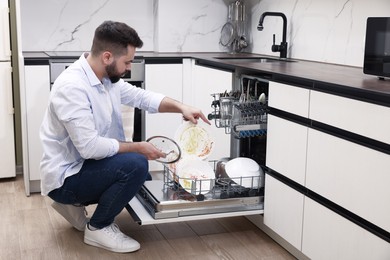 Photo of Man loading dishwasher with dirty plates indoors