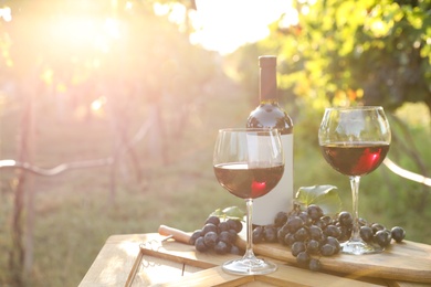 Photo of Composition with wine and ripe grapes on wooden table in vineyard