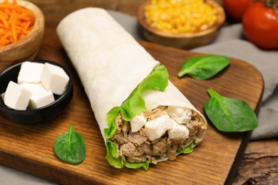 Delicious tortilla wrap with tuna on wooden table