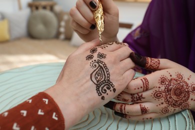 Photo of Professional mehndi master making henna tattoo indoors, closeup